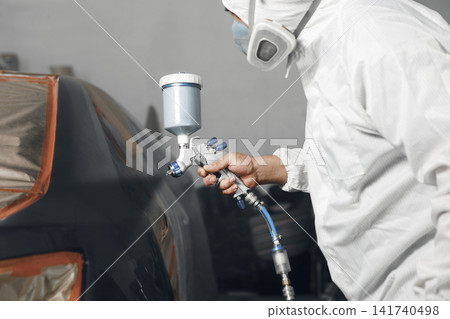 Car service male worker sprays dye on the elements part of car. Car body painting. Recovery of the car after the accident. 141740498