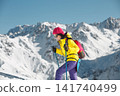 Woman Engaged in Winter Hiking With Trekking Poles Amidst Snow-Covered Mountain Range 141740499