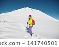 Smiling Woman Ascending Mountain Peak With Trekking Poles Against Clear Blue Sky 141740501