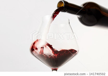 Red wine pouring into tilted wineglass from bottle. Red wine pouring into tilted wineglass from bottle. 141740502