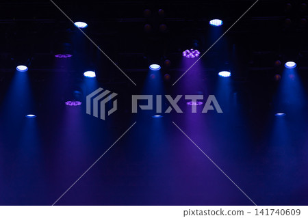 Blue and purple spotlights cut through atmospheric haze above an empty concert stage Blue and purple spotlights cut through atmospheric haze above an empty concert stage 141740609