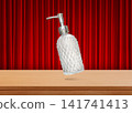 A clear glass perfume bottle with a diamond pattern sits on a wooden table, with a red curtain as a backdrop. 141741413
