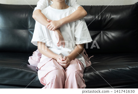 Younger sister hugging her older sister on a black leather sofa, expressing sibling love, affection, family bonding, and childhood togetherness. Younger sister hugging her older sister on a black leather sofa, expressing sibling love, affection, family bonding, and childhood togetherness. 141741630