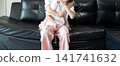 Playful sisters relaxing at home share a cheerful hug on the living room sofa, capturing joyful childhood moments, fun interaction, and everyday family lifestyle. 141741632