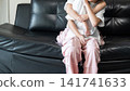 Younger sister hugging her older sister on a black leather sofa, expressing sibling love, affection, family bonding, and childhood togetherness at home. 141741633