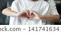 Younger sister hugs her older sister from behind while making a heart shape with her hands, expressing love, affection, and family bonding. 141741634