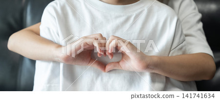 Younger sister hugs her older sister from behind while making a heart shape with her hands, expressing love, affection, and family bonding. Younger sister hugs her older sister from behind while making a heart shape with her hands, expressing love, affection, and family bonding. 141741634