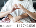 Older sister makes a heart shape with her hands while her younger sister hugs her from behind, expressing love, trust, and family bonding. 141741636