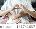 An older sister forms a heart with her hands as her younger sister embraces her from behind, symbolizing care, unity, and emotional connection. 141741637