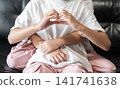 A younger sister hugs her older sister from behind while the older sister makes a heart sign, representing unconditional love and emotional support. 141741638