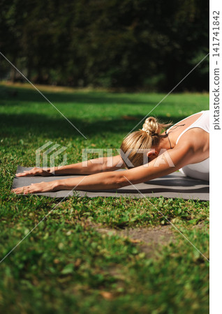 Woman Stretching Forward on a Yoga Mat in a Park Woman Stretching Forward on a Yoga Mat in a Park 141741842