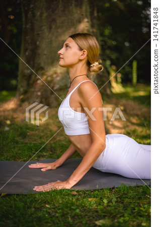 Woman in Cobra Yoga Pose on a Mat in a Park Woman in Cobra Yoga Pose on a Mat in a Park 141741848