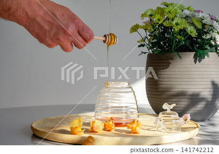 Drizzling Honey from a Wooden Dipper into a Jar 141742212