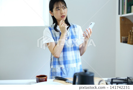 Kitchen - Image of a woman thinking up recipes on her smartphone. Kitchen - Image of a woman thinking up recipes on her smartphone. 141742231