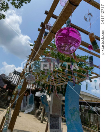 Pink wind chimes against a blue sky and a summer landscape Pink wind chimes against a blue sky and a summer landscape 141742757
