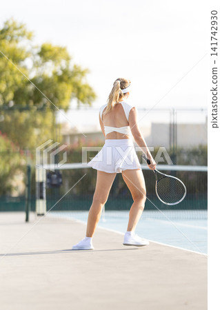 Tennis player preparing to serve on a court during the day in a sunny setting Tennis player preparing to serve on a court during the day in a sunny setting 141742930