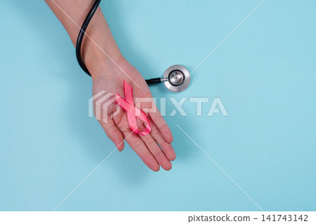 Hand holding pink ribbon next to stethoscope for breast cancer medical awareness Hand holding pink ribbon next to stethoscope for breast cancer medical awareness 141743142