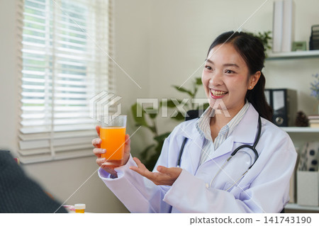 Smiling Asian female doctor holding glass of orange juice during nutrition consultation Smiling Asian female doctor holding glass of orange juice during nutrition consultation 141743190