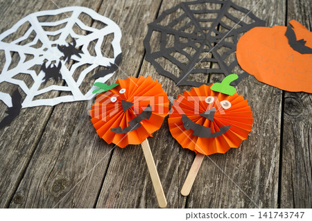 High angle shot of two completed handmade paper pumpkin jack-o'-lanterns on sticks over wooden background High angle shot of two completed handmade paper pumpkin jack-o'-lanterns on sticks over wooden background 141743747
