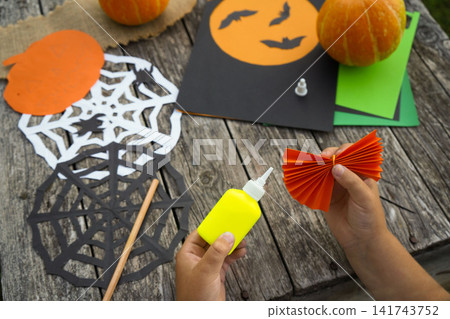 Little girl using a yellow glue bottle while assembling a handmade paper pumpkin decoration outdoors Little girl using a yellow glue bottle while assembling a handmade paper pumpkin decoration outdoors 141743752