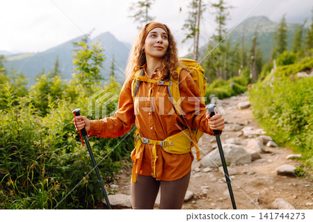 Woman travels along hiking trails among mountains with yellow backpack and hiking boots. Vacation. Woman travels along hiking trails among mountains with yellow backpack and hiking boots. Vacation. 141744273
