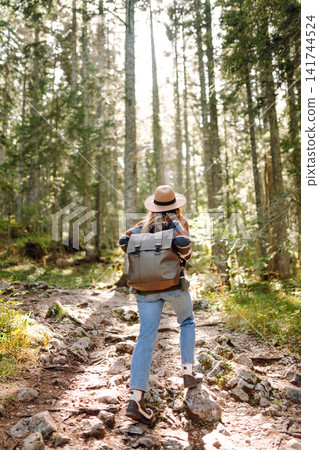Woman with backpack hiking outdoors in the Forest. Trekking in the Pine Woods. Hiking lifestyle Woman with backpack hiking outdoors in the Forest. Trekking in the Pine Woods. Hiking lifestyle 141744524