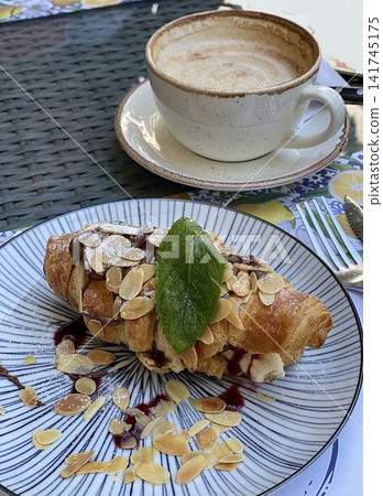 Fresh croissant with almond flakes and cream filling served with a cup of coffee Fresh croissant with almond flakes and cream filling served with a cup of coffee 141745175
