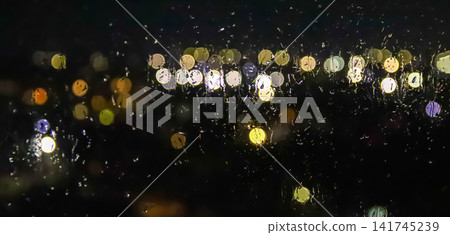Atmospheric night city view through a rain-streaked window with blurred bokeh lights, melancholic urban background and rainy weather concept Atmospheric night city view through a rain-streaked window with blurred bokeh lights, melancholic urban background and rainy weather concept 141745239