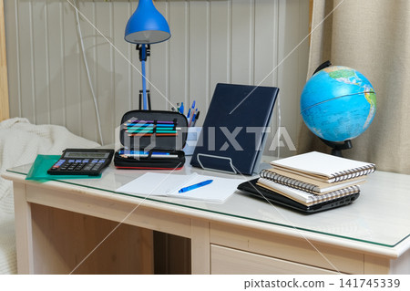 Organized home office desk layout for distance e learning or IT freelance. Open laptop, blue wireless headphones, table lamp, pen organizer on tabletop. Tech driven Workspace. Minimalist Student Desk. Organized home office desk layout for distance e learning or IT freelance. Open laptop, blue wireless headphones, table lamp, pen organizer on tabletop. Tech driven Workspace. Minimalist Student Desk. 141745339
