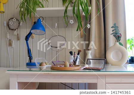 Modern makeup table with cosmetics and mirror on wooden desk. Eyeshadow palettes, beauty blenders, makeup brushes, perfume bottle on table. Concept of self care. Beauty Routine, Everyday Makeup Setup Modern makeup table with cosmetics and mirror on wooden desk. Eyeshadow palettes, beauty blenders, makeup brushes, perfume bottle on table. Concept of self care. Beauty Routine, Everyday Makeup Setup 141745361