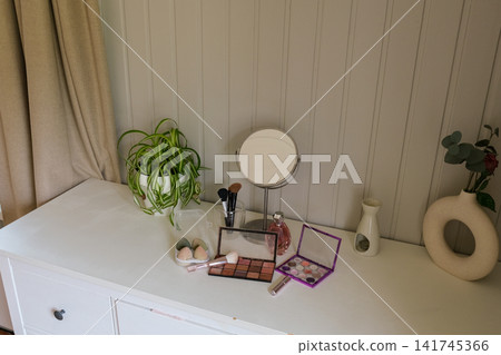 Modern makeup table with cosmetics and mirror on wooden desk. Eyeshadow palettes, beauty blenders, makeup brushes, perfume bottle on table. Concept of self care. Beauty Routine, Everyday Makeup Setup Modern makeup table with cosmetics and mirror on wooden desk. Eyeshadow palettes, beauty blenders, makeup brushes, perfume bottle on table. Concept of self care. Beauty Routine, Everyday Makeup Setup 141745366