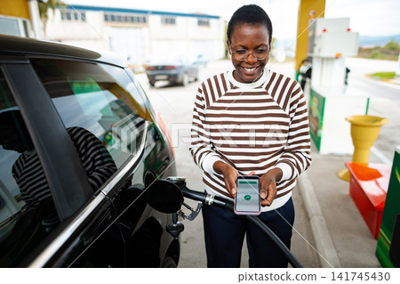 Woman paying for gasoline using mobile phone at gas station Woman paying for gasoline using mobile phone at gas station 141745430