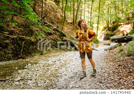 A traveler walks along forest hiking trail in mountains on a sunny day. Outdoor recreation concept. A traveler walks along forest hiking trail in mountains on a sunny day. Outdoor recreation concept. 141745440