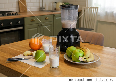 Electric blender on kitchen counter for smoothie making process. Fresh fruits, cutting board, and glass of protein milkshake on table. Healthy lifestyle. Vitamin Boost, Morning Routine and Self Care Electric blender on kitchen counter for smoothie making process. Fresh fruits, cutting board, and glass of protein milkshake on table. Healthy lifestyle. Vitamin Boost, Morning Routine and Self Care 141745459