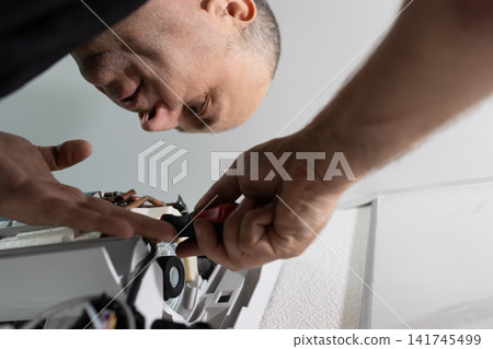 Repairman fixing indoor air conditioner unit with screwdriver. Professional HVAC technician at work. Repairman fixing indoor air conditioner unit with screwdriver. Professional HVAC technician at work. 141745499