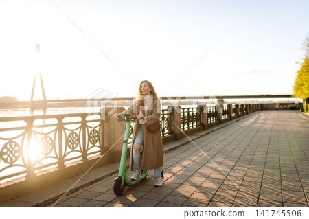 Woman driving electric scooter along the waterfront. Active life. Ecological transportation concept. 141745506