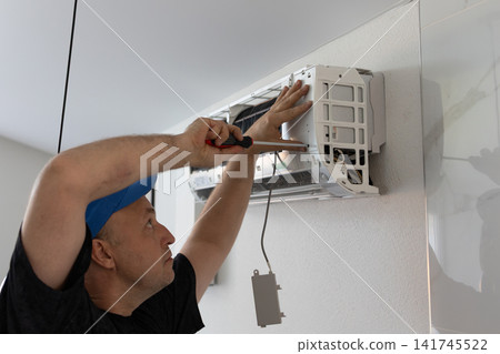 Repairman fixing wall air conditioner with screwdriver. Maintenance and professional service of climate system. Repairman fixing wall air conditioner with screwdriver. Maintenance and professional service of climate system. 141745522