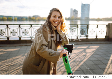 Woman driving electric scooter along the waterfront. Active life. Ecological transportation concept. Woman driving electric scooter along the waterfront. Active life. Ecological transportation concept. 141745528