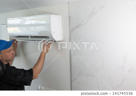 Technician repairing air conditioner on wall. Professional worker fixing climate control system unit. Technician repairing air conditioner on wall. Professional worker fixing climate control system unit. 141745536