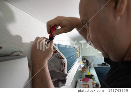 Technician repairing air conditioner with screwdriver. Professional maintenance service in home interior. Technician repairing air conditioner with screwdriver. Professional maintenance service in home interior. 141745539
