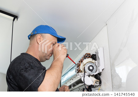 Technician fixing indoor air conditioner unit with screwdriver. Repair service for cooling system home. Technician fixing indoor air conditioner unit with screwdriver. Repair service for cooling system home. 141745540