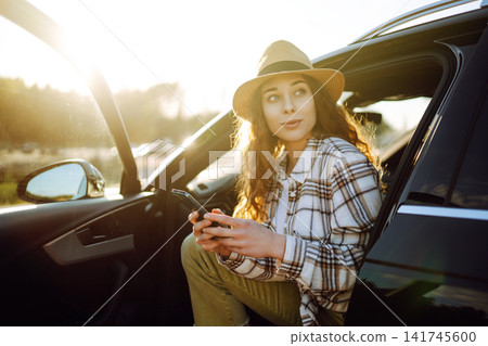 Woman enjoying sunny day by lake while checking phone next to parked car. Travel, weekend concept Woman enjoying sunny day by lake while checking phone next to parked car. Travel, weekend concept 141745600