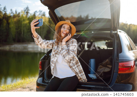 Young Woman is resting in trunk of car, taking selfie. Travel, weekend, relax and lifestyle concept. Young Woman is resting in trunk of car, taking selfie. Travel, weekend, relax and lifestyle concept. 141745603