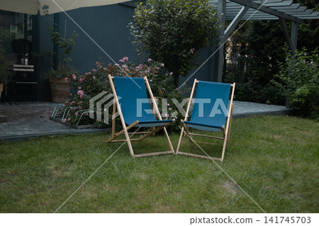 Two blue folding deck chairs on green lawn in backyard 141745703