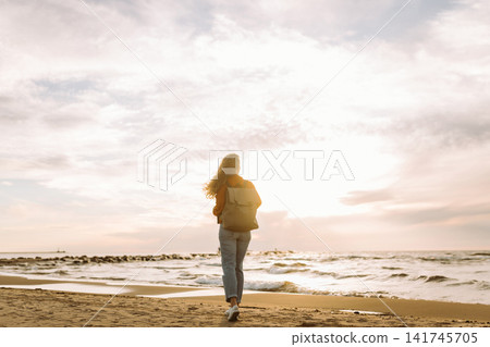 Beautiful woman on beach at sunset. Cold weather. Tourist, active lifestyle, relax concept. Beautiful woman on beach at sunset. Cold weather. Tourist, active lifestyle, relax concept. 141745705