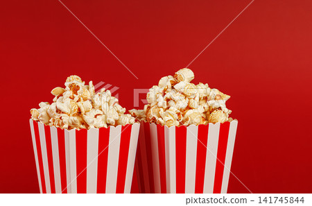 Horizontal shot of two popcorn buckets on red backdrop. Minimalist food background. Horizontal shot of two popcorn buckets on red backdrop. Minimalist food background. 141745844