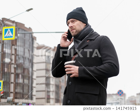 Bearded adult man using smartphone outdoors city street. Focused male looking at mobile phone screen, city road background, winter autumn commute. Urban Mobile Tech Digital Lifestyle. Remote Business Bearded adult man using smartphone outdoors city street. Focused male looking at mobile phone screen, city road background, winter autumn commute. Urban Mobile Tech Digital Lifestyle. Remote Business 141745915