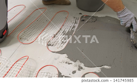 Worker installing electric underfloor heating system mat. Underfloor Heating Installation. Builder applying concrete mortar adhesive with trowel on cables. Energy Efficiency, Smart Home Foundation. Worker installing electric underfloor heating system mat. Underfloor Heating Installation. Builder applying concrete mortar adhesive with trowel on cables. Energy Efficiency, Smart Home Foundation. 141745985