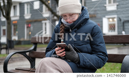 Teenage girl talking smartphone in blurry city park. Young teen female having phone call conversation. Gen Z Youth Communication. Authentic Everyday City Realities. Chilly Weather. Cozy Street Style Teenage girl talking smartphone in blurry city park. Young teen female having phone call conversation. Gen Z Youth Communication. Authentic Everyday City Realities. Chilly Weather. Cozy Street Style 141746000