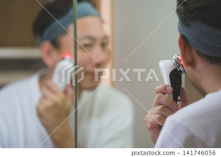 一名 40 歲男子在浴室鏡子前使用多功能臉部護理儀進行男士護理。 一名 40 歲男子在浴室鏡子前使用多功能臉部護理儀進行男士護理。 141746056